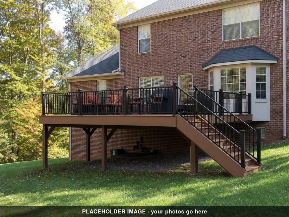 Raised deck with black metal railing and stairs beside a brick house, patio chairs on top (placeholder image)
